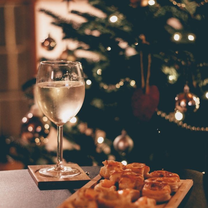 Glas Wein neben festlich dekorierten Plätzchen vor einem geschmückten Weihnachtsbaum.